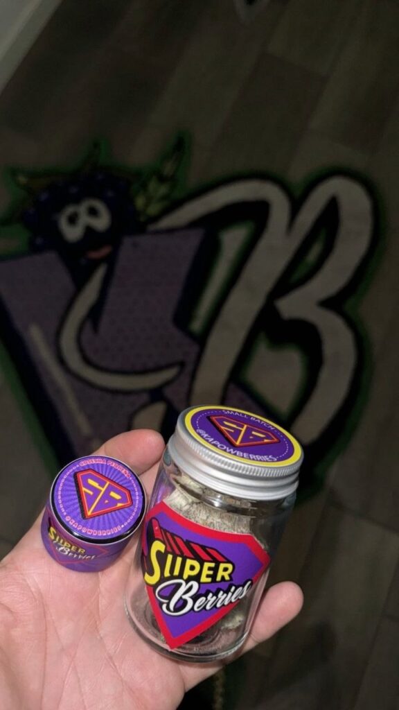 Close-up photo of purple-dusted cannabis buds from the Kapow "Super Berries" strain, showing rich trichome coverage and a dense structure.